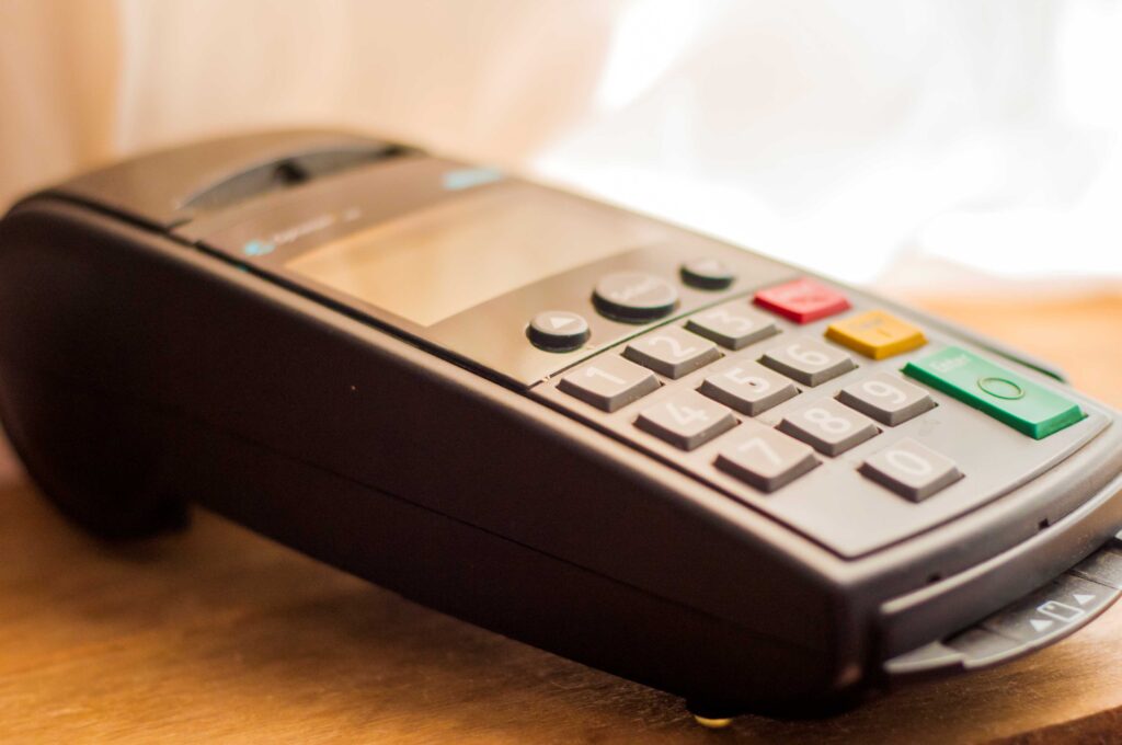 A close-up of a traditional POS terminal with physical buttons, sitting on a wooden counter, ready for a card payment.