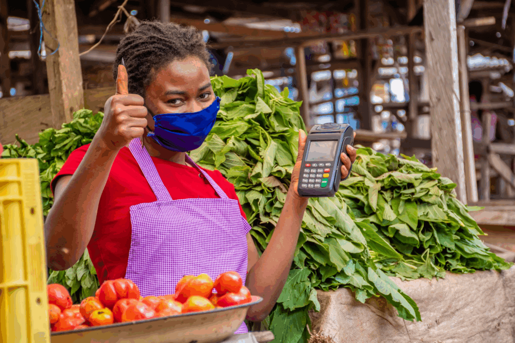 A Nigerian market vendor smiles while holding a mobile POS (mPOS), showing how different types of POS empower small merchants.
