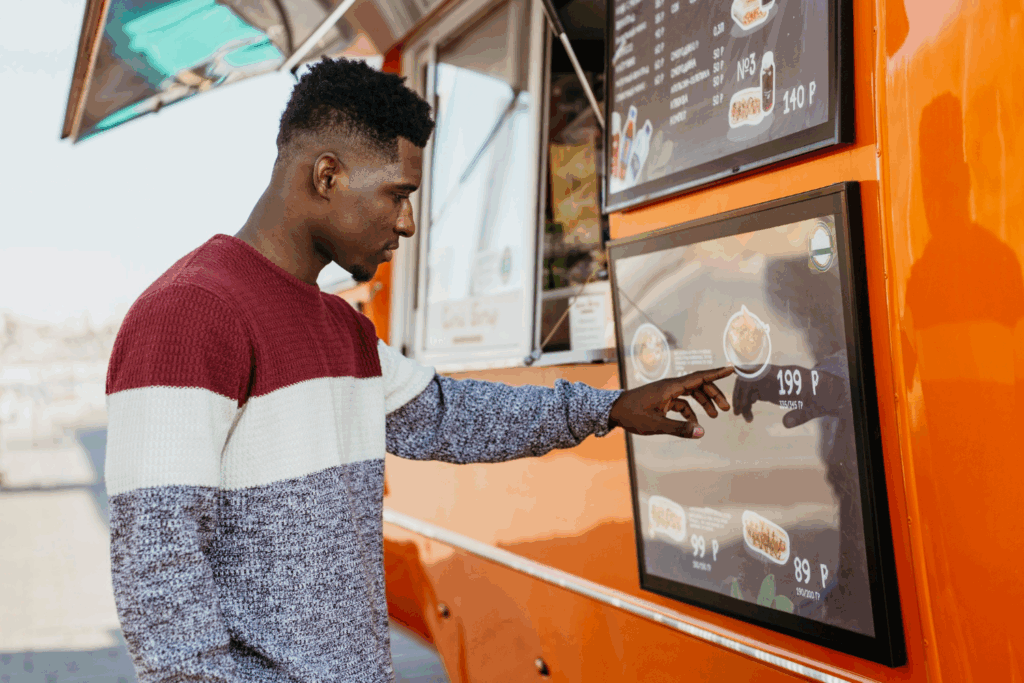 A customer using a self-service kiosk on a food truck, an interactive type of POS system that speeds up ordering.
